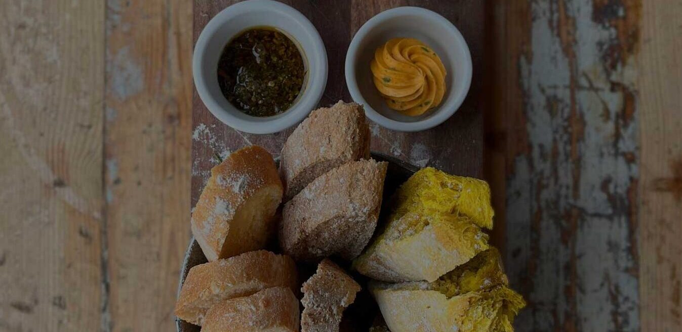 Verschiedene Brotsorten mit vier Dips auf Holzbrett angerichtet. Rustikaler Holztisch als Untergrund